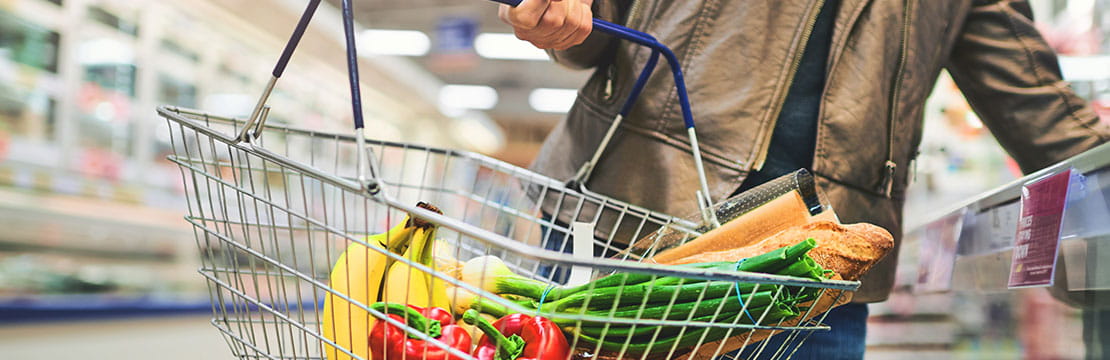 Person holding a shopping basket filled with organic produce in a grocery store aisle.