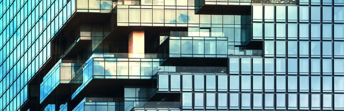 View of modern glass building with staggered balconies and reflective windows.